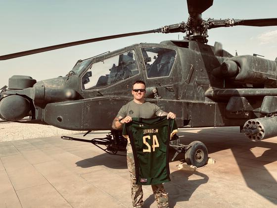 Nick Giusti holds up a McDaniel football jersey in front of a helicopter while stationed in Syria.