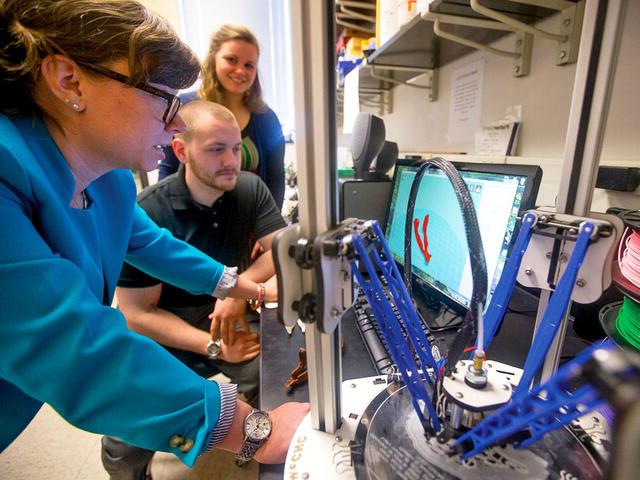 Biology professor guiding students in 3D printing.