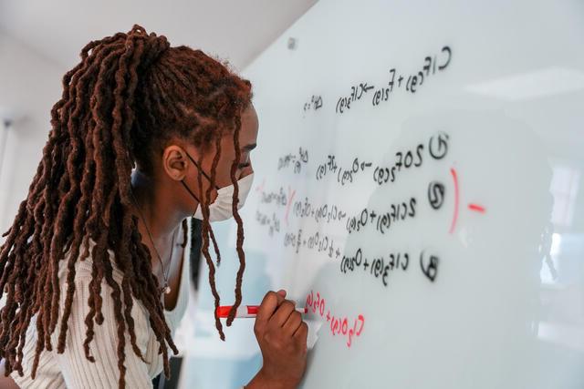 Student writes math equations on a whiteboard.