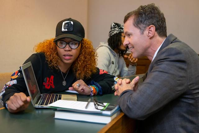 A Black, female student speaks to a white man while they look at a laptop screen.