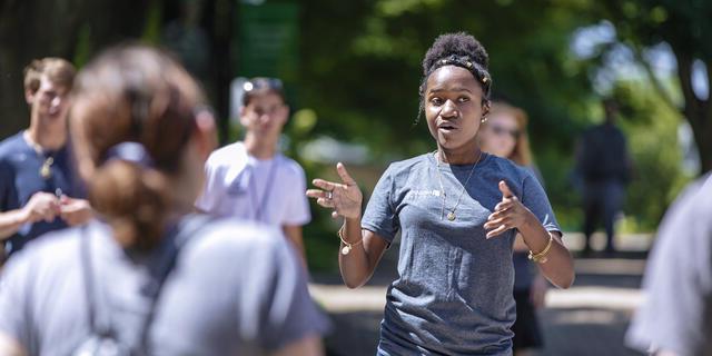 A students speaks to a group of other students outside on campus.